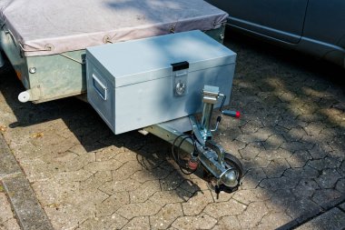 Alçak bir römork sağlam bir top çekme montajı ve yedek parçaları gösterir. Çerçevesi boyunca tutacakları olan büyük gri metal bir yan kutu, hareket halindeki ekipmanları depolamaya hazır..