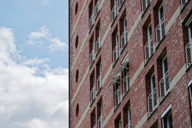 A brick facade rises on a new build, rows of small door openings lead to shallow guards like mini balconies, there is only a narrow ledge before the rail, the site is unfinished and repeating