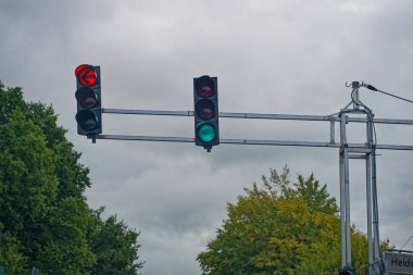 Yolun yukarısında iki işaret asılı, sol ok virajı engelleyen kırmızı ışığı gösteriyor, merkez baş trafik, gece rengi ve yansımalar için yeşili gösteriyor sakin kavşağı işaret ediyor