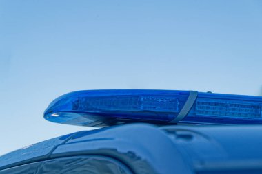 A close view shows a blue police lightbar on the roof, the lens is clear and bright, metal mounts hold it steady, it signals duty and response, the sky reflects softly across the smooth housing