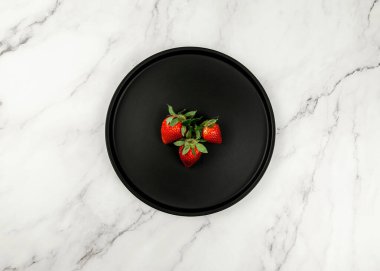 Beyaz mermer zemin üzerinde siyah plaka üst görünümü. Üç tane düz çilek. Boşluğu kopyala.