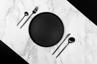 Siyah çatal bıçak takımı ve siyah plaka beyaz mermer arka planda. Yaratıcı masa düzleştirici. Siyah ve mermer, boşluğu kopyala.