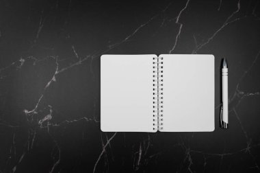Siyah mermer zemin üzerinde beyaz defter ve kalem üst görünümü. Düz yat, boşluğu kopyala.