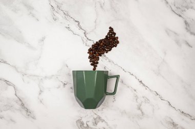 Beyaz mermer arka plandaki kahve fincanının üst görüntüsü. Kahve çekirdekleri ve yeşil fincanlar düzdü. Boşluğu kopyala.