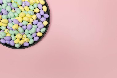 Pembe arka planda siyah tabakta renkli paskalya yumurtalarının üst görüntüsü. Yaratıcı paskalya kompozisyonu, yay, kopyalama alanı, düz konum.