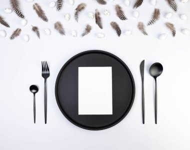 Kahverengi tüylerin üst görüntüsü, beyaz arka planda beyaz paskalya yumurtaları. Masa takımı, beyaz kart, siyah tabak ve çatal bıçak takımı. Yaratıcı paskalya kompozisyonu, yay, kopyalama alanı, düz konum. 