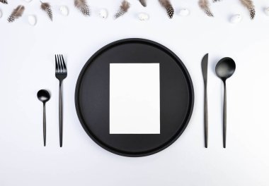 Kahverengi tüylerin üst görüntüsü, beyaz arka planda beyaz paskalya yumurtaları. Masa takımı, beyaz kart, siyah tabak ve çatal bıçak takımı. Yaratıcı paskalya kompozisyonu, yay, kopyalama alanı, düz konum. 