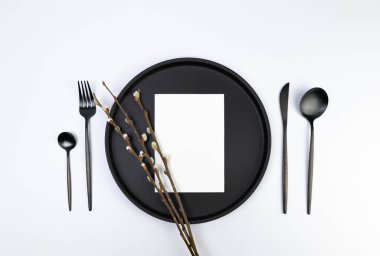 Top view of black plate and cutlery, white card, pussy willow branches on white background. Spring easter composition, copy space, flat lay.