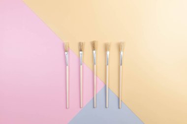 Renkli arka planda boya fırçalarının üst görüntüsü. Mavi, pembe ve sarı arka plan. Renkli duvar kağıdı, düz yatak, kopyalama alanı.