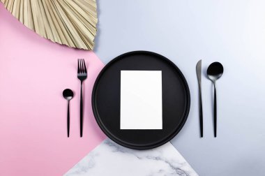 Siyah tabak ve çatal bıçak takımı, beyaz kart, renkli arka planda kurumuş palmiye yaprağı. Masa seti, mavi, pembe ve mermer arka plan. Pastel renkli duvar kağıdı, mermer doku, boşluğu kopyala.