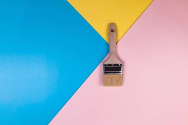 Renkli arka planda boya fırçasının üst görüntüsü. Mavi, pembe ve sarı arka plan. Renkli duvar kağıdı, düz yatak, kopyalama alanı.