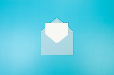 Açık mavi zarfın üst görüntüsü, mavi arka planda beyaz kart. Yat yere. Boşluğu kopyala.