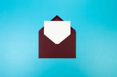 Koyu kırmızı zarfın üst görüntüsü, mavi arka planda beyaz kart. Yat yere. Boşluğu kopyala.