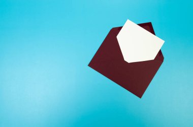 Koyu kırmızı zarfın üst görüntüsü, mavi arka planda beyaz kart. Yat yere. Boşluğu kopyala.