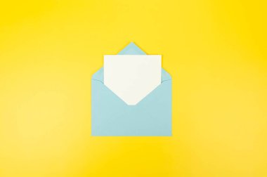 Açık mavi zarfın üst görüntüsü, sarı arka planda beyaz kart. Yat yere. Boşluğu kopyala.