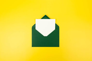 Koyu yeşil zarfın üst görüntüsü, sarı arka planda beyaz kart. Yat yere. Boşluğu kopyala.