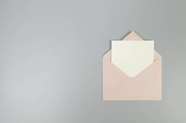 Pembe zarfın üst görüntüsü, gri arka planda beyaz kart. Yat yere. Boşluğu kopyala.