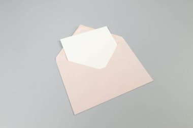 Pembe zarfın üst görüntüsü, gri arka planda beyaz kart. Yat yere. Boşluğu kopyala.