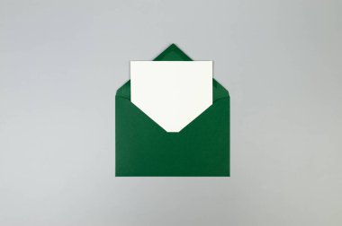 Yeşil zarfın üst görüntüsü, gri arka planda beyaz kart. Yat yere. Boşluğu kopyala.