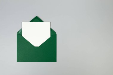 Yeşil zarfın üst görüntüsü, gri arka planda beyaz kart. Yat yere. Boşluğu kopyala.