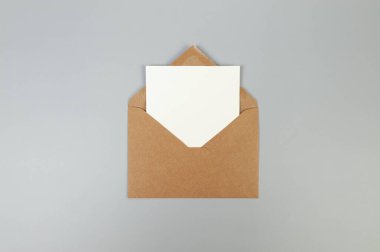 Kraft kahverengi zarfın üst görüntüsü, gri arka planda beyaz kart. Yat yere. Boşluğu kopyala.