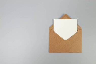 Kraft kahverengi zarfın üst görüntüsü, gri arka planda beyaz kart. Yat yere. Boşluğu kopyala.