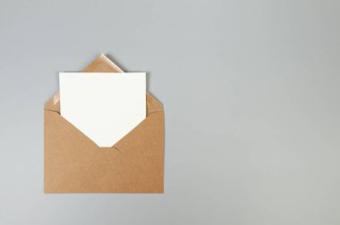 Kraft kahverengi zarfın üst görüntüsü, gri arka planda beyaz kart. Yat yere. Boşluğu kopyala.