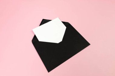 Siyah zarfın üst görüntüsü, pembe arka planda beyaz kart. Yat yere. Boşluğu kopyala.