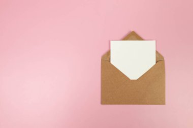 Kahverengi Kraft zarfının üst görüntüsü, pembe arka planda beyaz kart. Yat yere. Boşluğu kopyala.