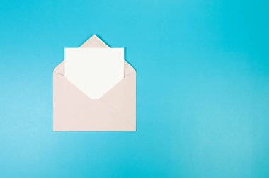 Açık pembe zarfın üst görüntüsü, mavi arka planda beyaz kart. Yat yere. Boşluğu kopyala.