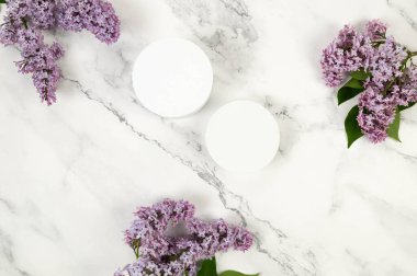 Beyaz mermer arka planda mor leylak çiçeklerinin üst görüntüsü. Ürün sunumu, beyaz tepsi, iki podyum. Yay duvar kağıdı, düz yatak, kopyalama alanı.