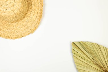 Hasır şapka ve beyaz arka planda kurumuş palmiye yaprağı manzarası. Yaz modası, tatil ve plaj duvar kâğıdı. Uzayı kopyala, düz yat.