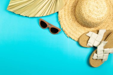Hasır şapka, kurutulmuş palmiye yaprağı, terlik ve mavi arka planda güneş gözlüğü. Yaz modası, tatil ve plaj duvar kâğıdı. Uzayı kopyala, düz yat.