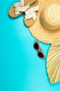 Hasır şapka, kurutulmuş palmiye yaprağı, terlik ve mavi arka planda güneş gözlüğü. Yaz modası, tatil ve plaj duvar kâğıdı. Uzayı kopyala, düz yat.