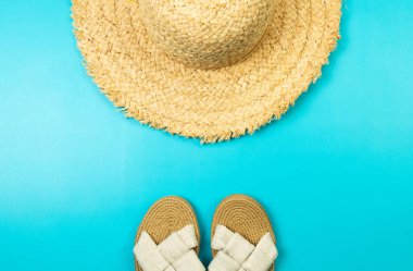 Mavi arka planda hasır şapka ve terliklerin üst görüntüsü. Yaz modası, tatil ve plaj duvar kâğıdı. Uzayı kopyala, düz yat.