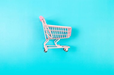 Mavi arka planda pembe alışveriş arabasının üst görüntüsü. Yaratıcı alışveriş duvar kâğıdı, satış. Uzayı kopyala, düz yat.