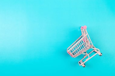 Mavi arka planda pembe alışveriş arabasının üst görüntüsü. Yaratıcı alışveriş duvar kâğıdı, satış. Uzayı kopyala, düz yat.