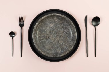 Kahverengi mermer plaka, siyah tabak ve pembe arka planda çatal bıçak. Yemek sunumu, taş tepsi. Tablo ayarı, kopyalama alanı, düz uzanma.