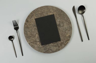 Kahverengi mermer plaka, siyah çatal bıçak takımı ve gri arka planda siyah kart. Yemek sunumu, taş tepsi. Tablo ayarı, kopyalama alanı, düz uzanma.