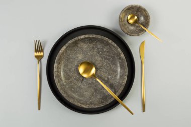Kahverengi mermer tabak ve kâse, siyah tabak ve gri arka planda altın çatal bıçak. Yemek sunumu, taş tepsi. Tablo ayarı, kopyalama alanı, düz uzanma.