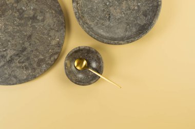 Sarı arka planda kahverengi mermer tepsi, tabak, kase ve altın çatal bıçak. Yemek sunumu, tabaklar, taş tepsi. Uzayı kopyala, düz yat.