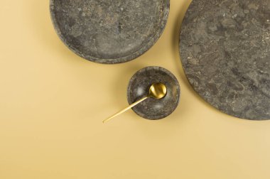 Sarı arka planda kahverengi mermer tepsi, tabak, kase ve altın çatal bıçak. Yemek sunumu, tabaklar, taş tepsi. Uzayı kopyala, düz yat.