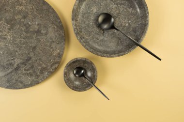 Sarı arka planda kahverengi mermer tepsi, tabak, kase ve siyah çatal bıçak. Yemek sunumu, tabaklar, taş tepsi. Uzayı kopyala, düz yat.