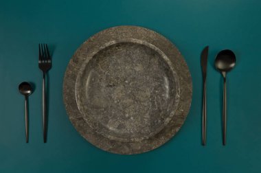 Kahverengi mermer tepsi ve tabağın üst görüntüsü, koyu yeşil arka planda siyah çatal bıçak takımı. Yemek sunumu, taş tepsi. Tablo ayarı, kopyalama alanı, düz uzanma.