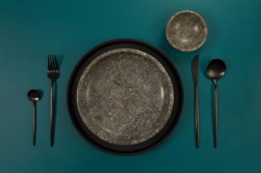 Kahverengi mermer tabak ve kâse, koyu yeşil arka planda siyah tabak ve çatal bıçak takımı. Yemek sunumu, taş tepsi. Tablo ayarı, kopyalama alanı, düz uzanma.