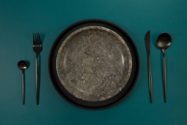 Kahverengi mermer plaka, siyah tabak ve koyu yeşil arka planda çatal bıçak. Yemek sunumu, taş tepsi. Tablo ayarı, kopyalama alanı, düz uzanma.
