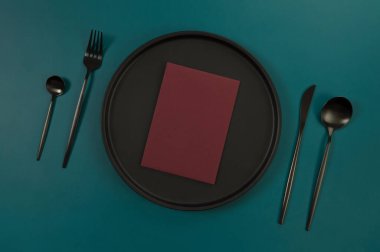 Siyah plaka, siyah çatal bıçak takımı ve koyu yeşil arka planda kırmızı kart. Yemek sunumu, siyah tepsi. Tablo ayarı, kopyalama alanı, düz uzanma.