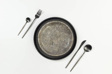 Kahverengi mermer plaka, siyah tabak ve beyaz arka planda çatal bıçak. Yemek sunumu, taş tepsi. Tablo ayarı, kopyalama alanı, düz uzanma.