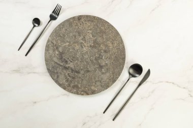 Kahverengi mermer plakanın üst manzarası, beyaz mermer arka planda siyah çatal bıçak takımı. Yemek sunumu, taş tepsi. Tablo ayarı, kopyalama alanı, düz uzanma.