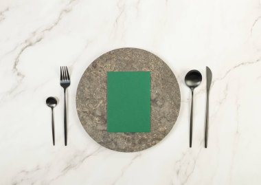 Kahverengi mermer plaka, siyah çatal bıçak takımı ve beyaz mermer arka planda yeşil kart. Yemek sunumu, taş tepsi. Tablo ayarı, kopyalama alanı, düz uzanma.